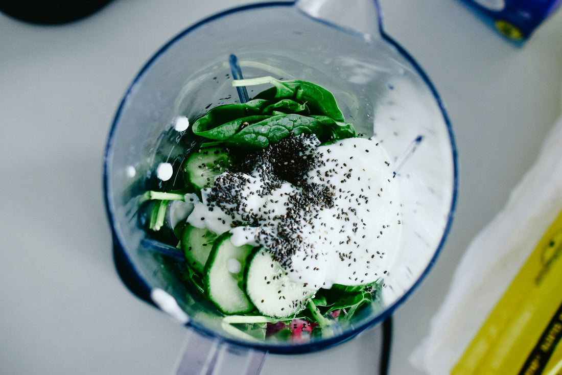 Blender jar filled with fresh spinach, cucumber, yogurt, and seeds on a kitchen counter