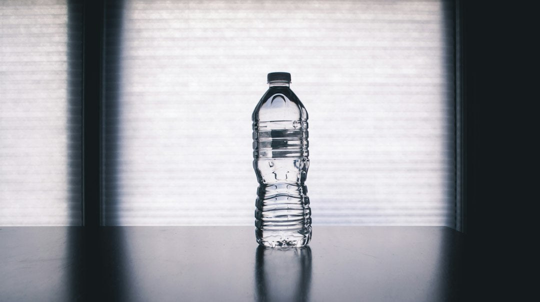 Clear reusable water bottle filled with water on a light background