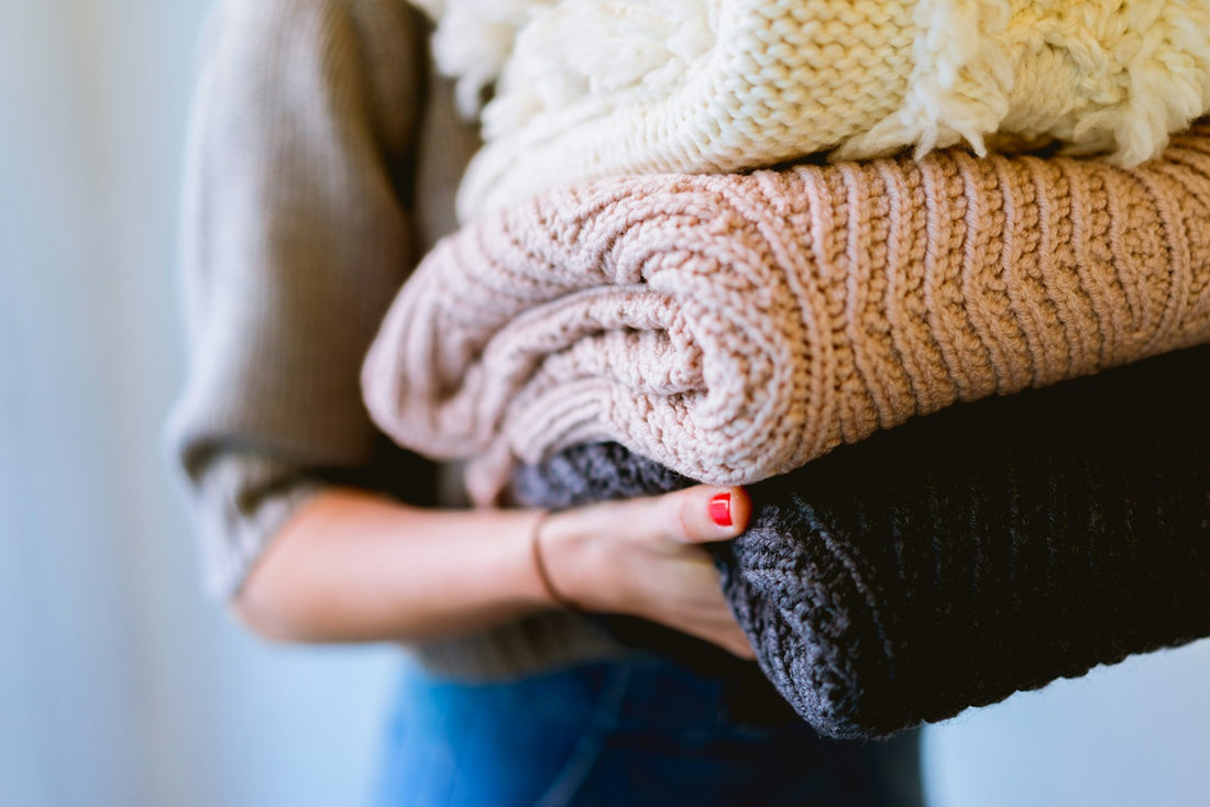 A person holding a neatly folded stack of knitted clothes