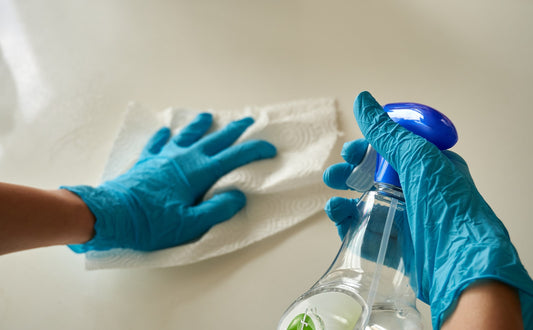 Gloved hands wiping a white surface with a cleaning cloth