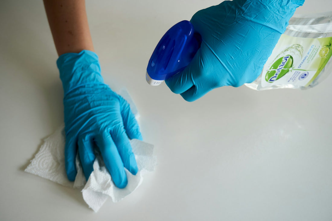 A person wearing blue gloves wiping a white household surface