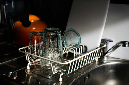 Clear glass mugs drying on a white metal dish rack
