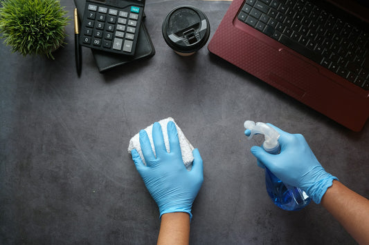 Gloved hands cleaning a desk with a spray bottle and cloth