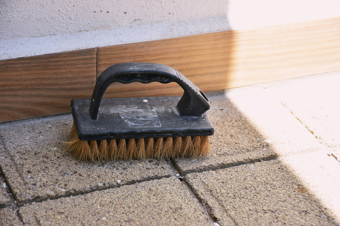A black-handled scrubbing brush resting on paving stones
